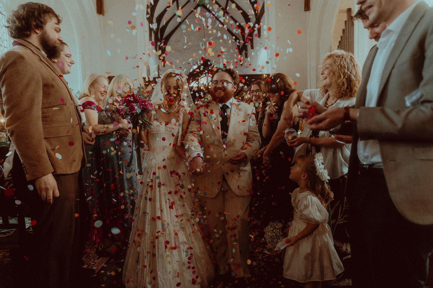Newlyweds walk down the aisle in a church as guests shower them with colorful confetti during their wedding ceremony.