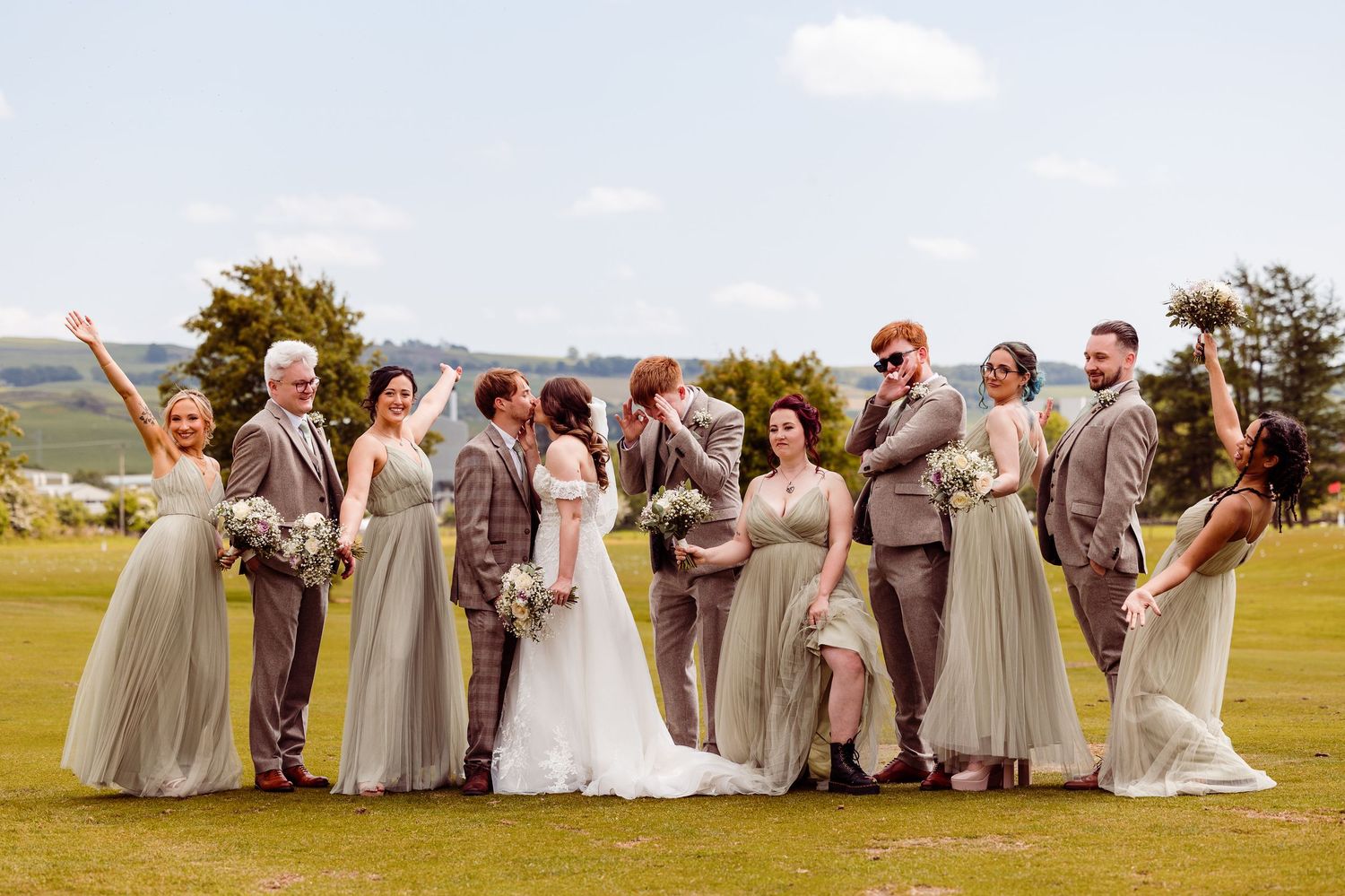 Bride and groom standing in a wildflower meadow surrounded by lush green trees under a cloudy sky.