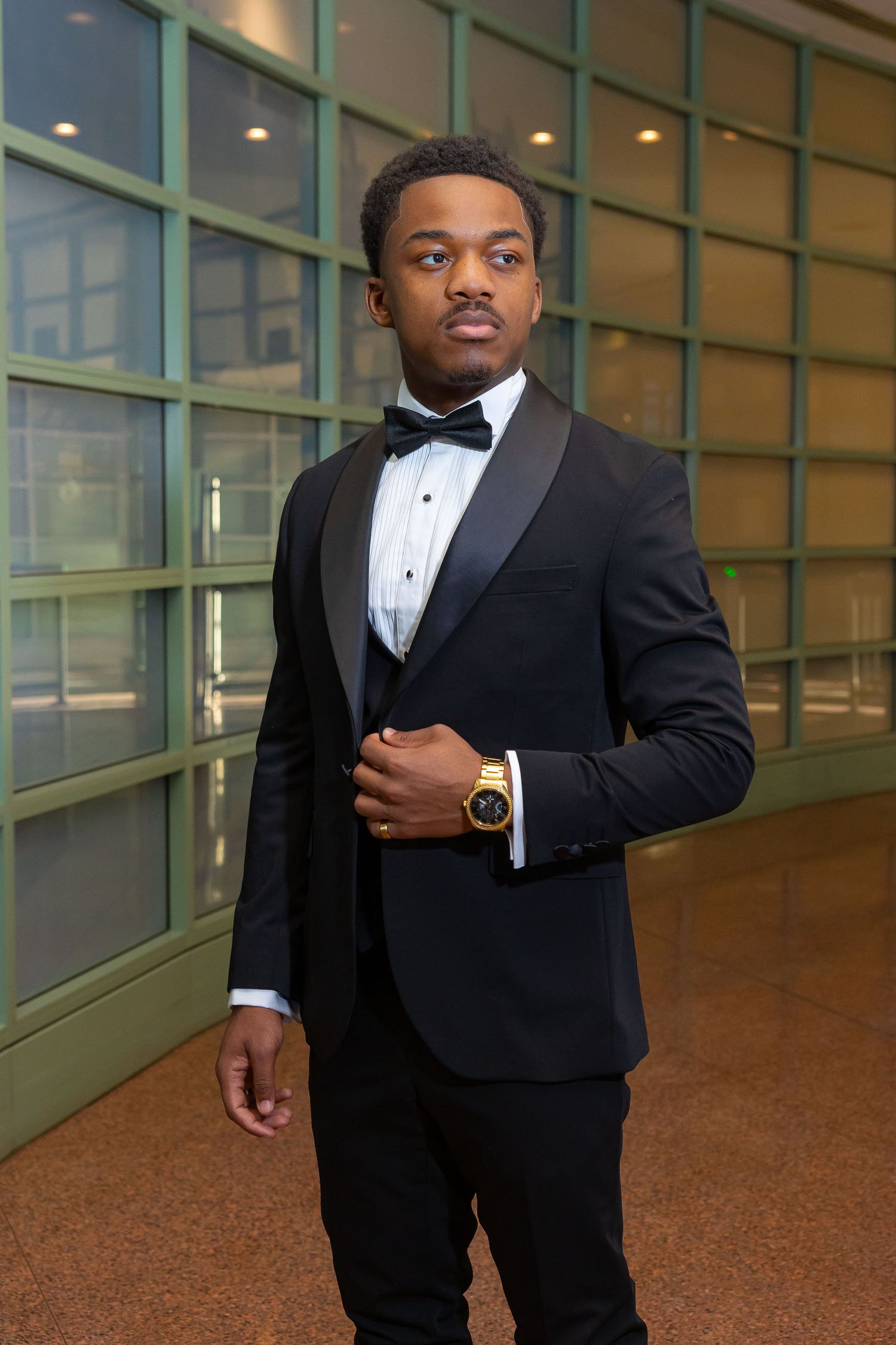A person wearing a dark suit stands in a modern building hallway with curved glass walls and polished floors.