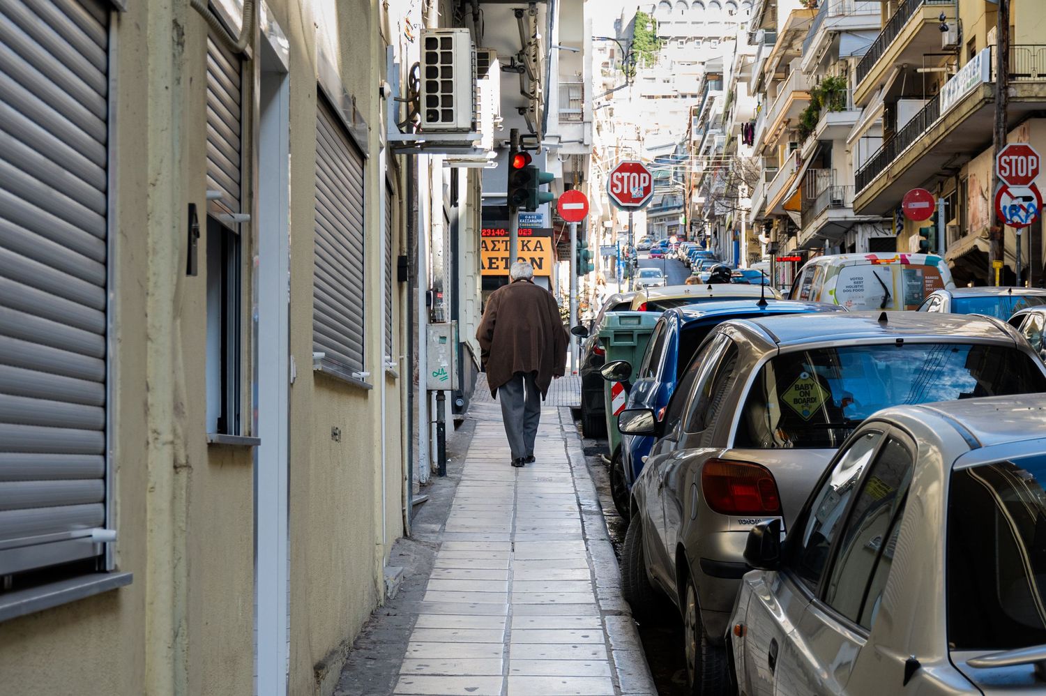 Narrow cobblestone street between old buildings with parked cars and pedestrians in a European city neighborhood.