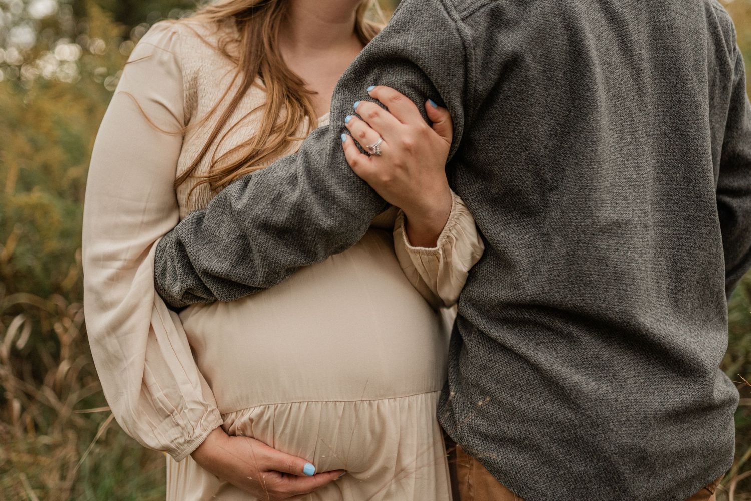A couple in neutral-toned clothing embraces during an outdoor autumn photoshoot.