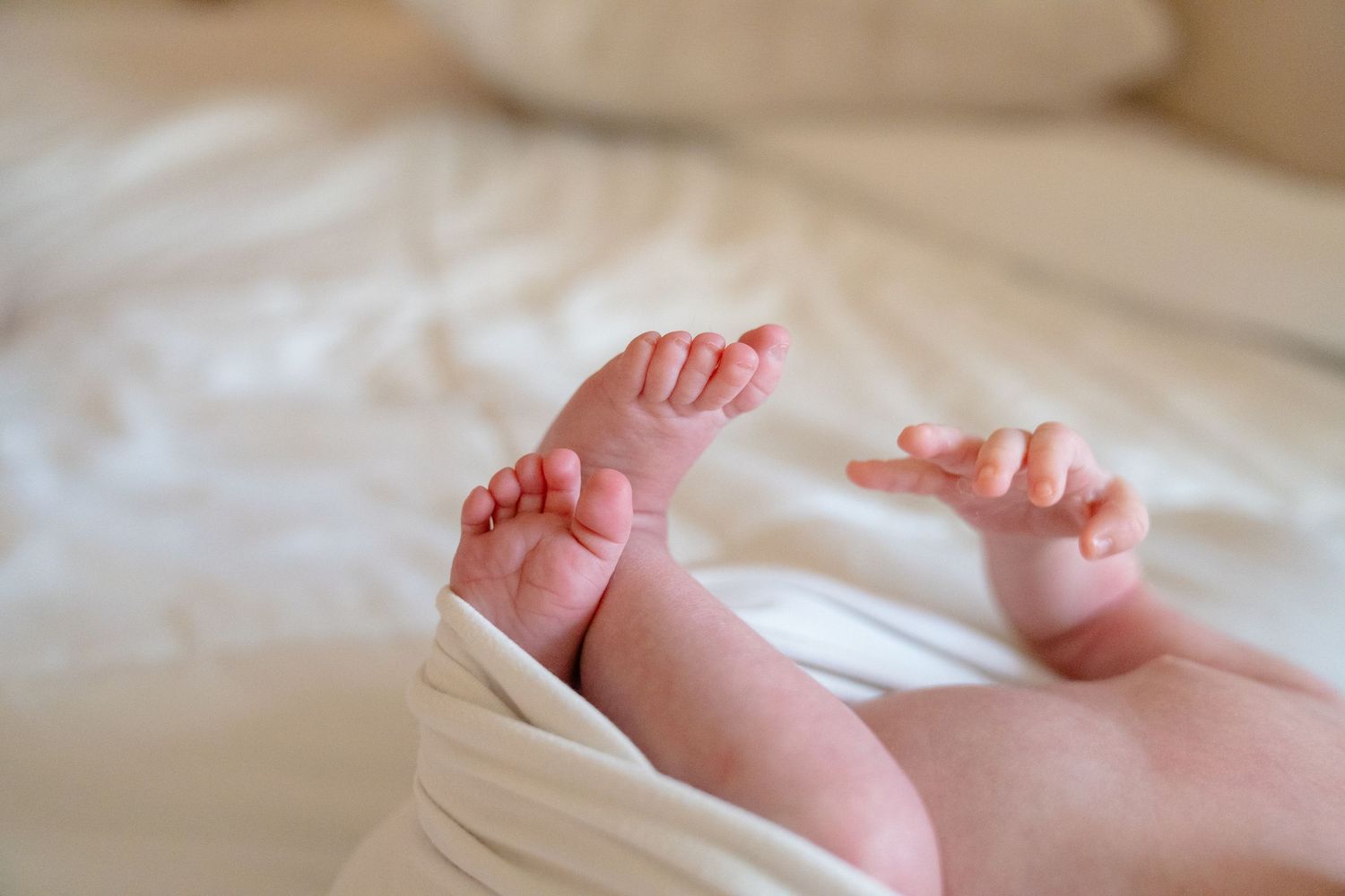 Close-up of a newborn baby's tiny feet and hands resting on a soft white blanket.