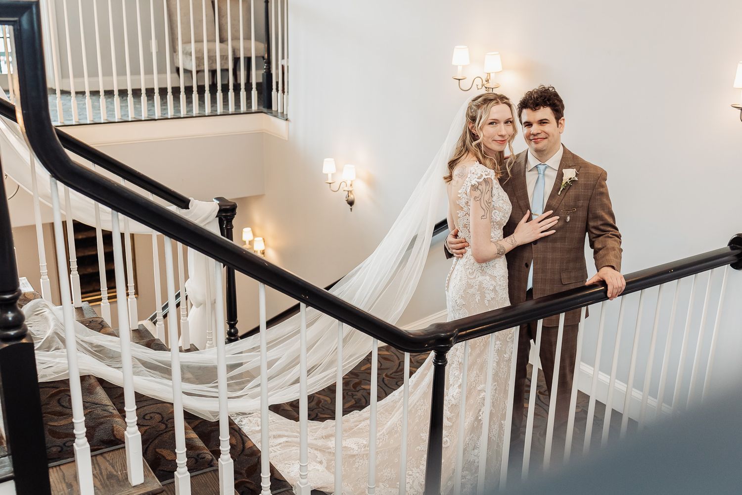 Bride and groom pose elegantly on a grand staircase, her flowing veil cascading down the steps.