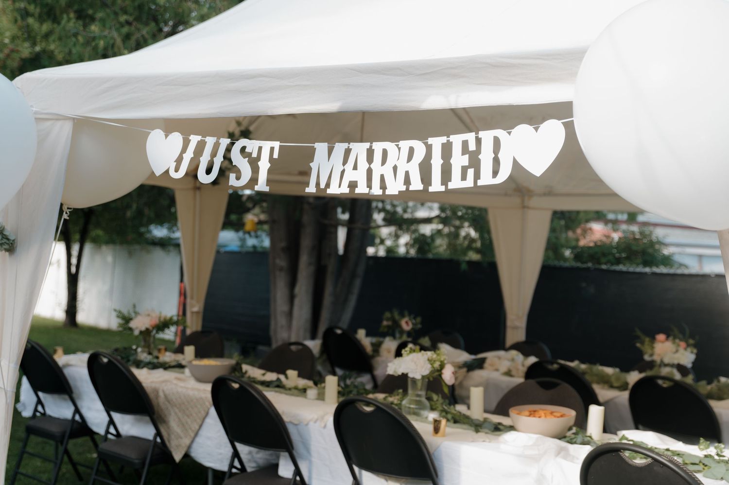 Just Married banner hanging under a white tent over elegantly decorated wedding reception tables with floral centerpieces.