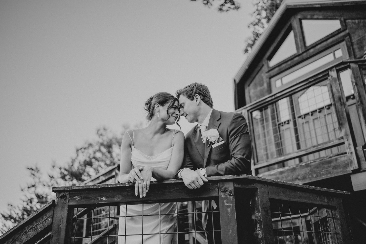 A couple shares a romantic kiss on a rustic wooden balcony in a black and white wedding photo.
