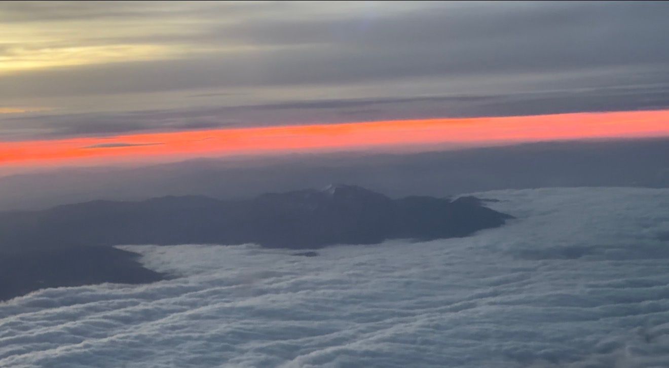 Aerial view of misty mountain islands at sunset with vibrant red and orange horizon glowing beneath dramatic cloud layers.