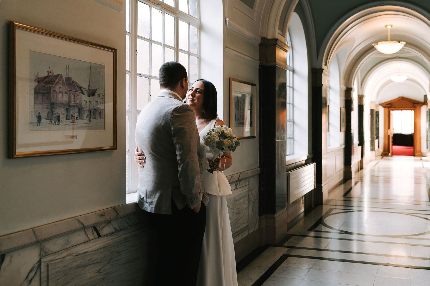 Bride and groom share a romantic moment by a window in an elegant hallway with arched ceilings at Islington Town Hall in London
