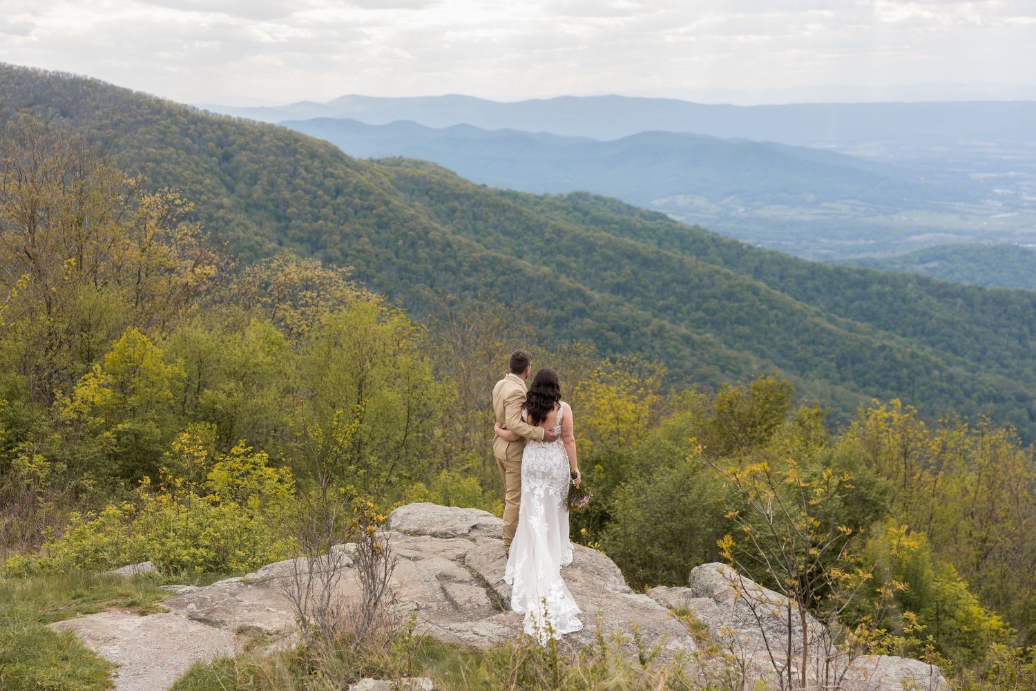 Newlywed couple walking hand in hand on a sunny park path, bride in white gown and groom in military dress uniform.