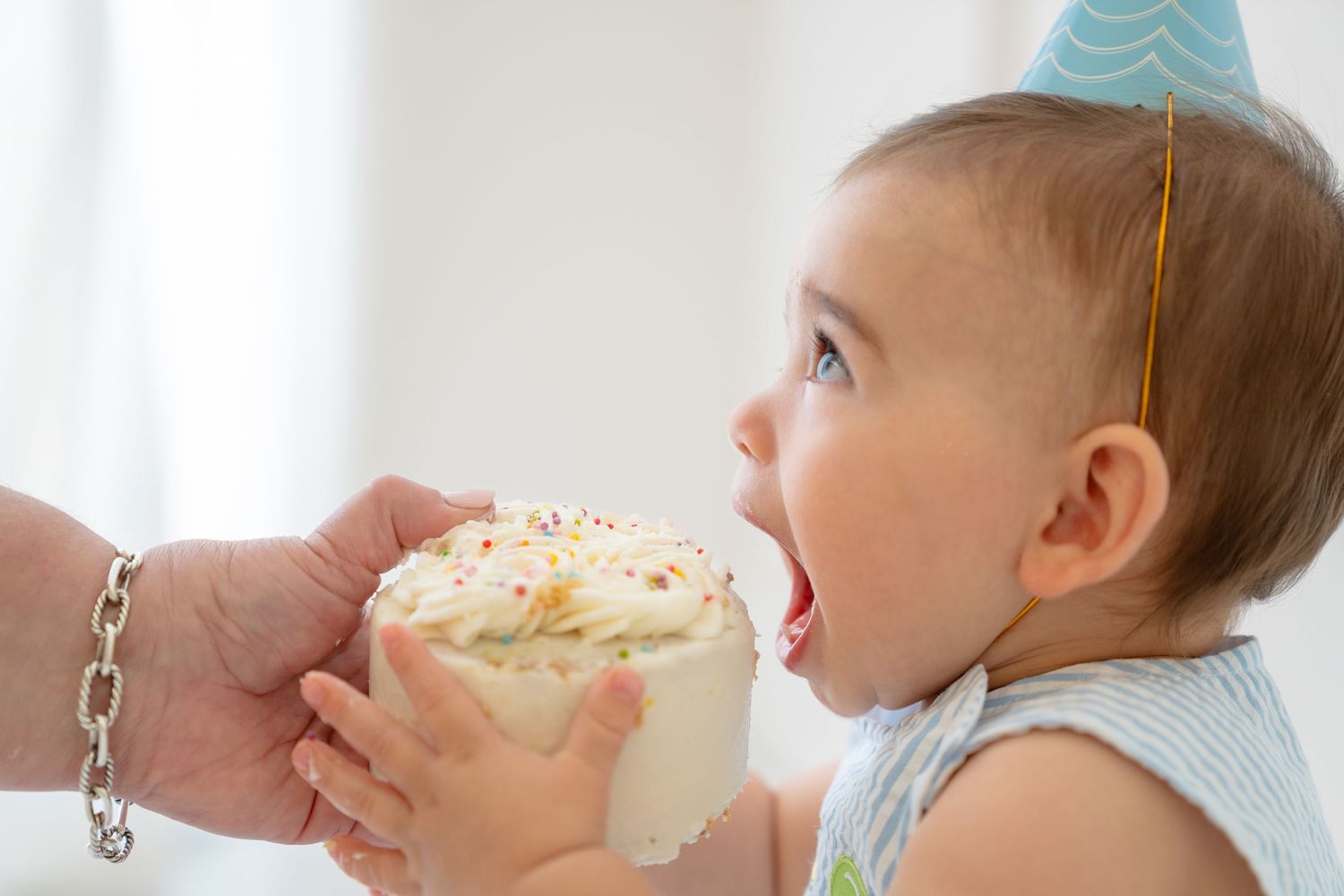 Baby in party hat eagerly eating birthday cake smash, celebrating first birthday milestone.