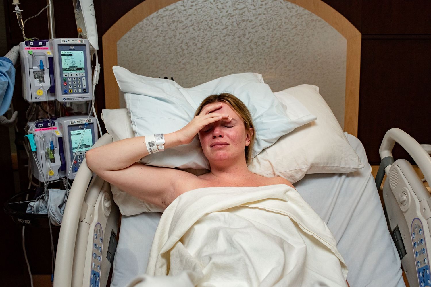 Person lying in a hospital bed with medical equipment visible in the background.