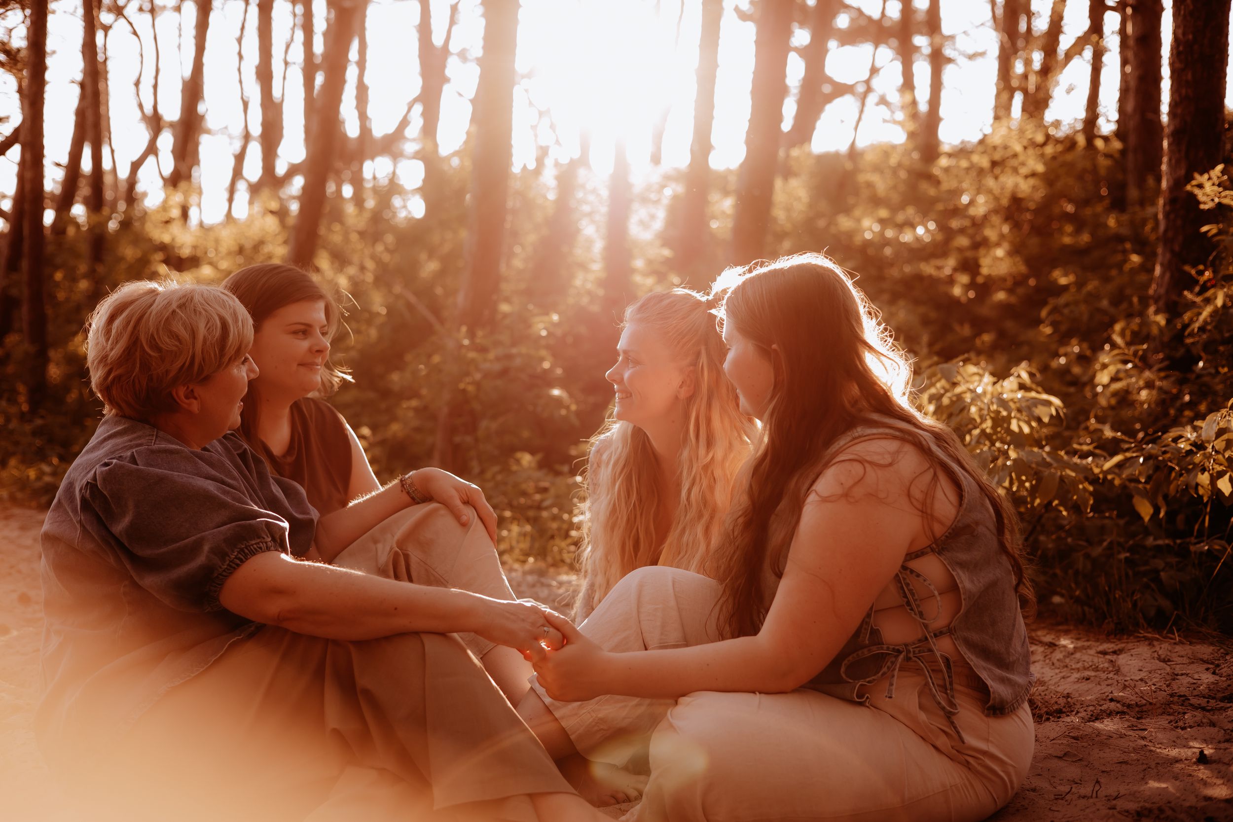 A group of four people laugh and relax together in a sunlit forest during golden hour.