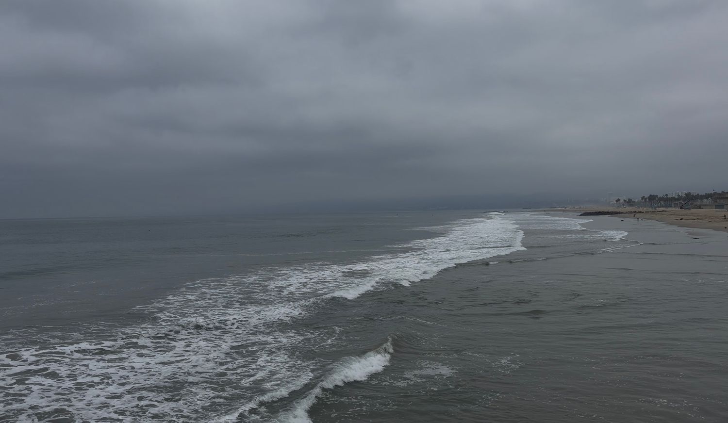 Aerial view of stormy ocean waves crashing on a sandy beach under dark overcast skies.