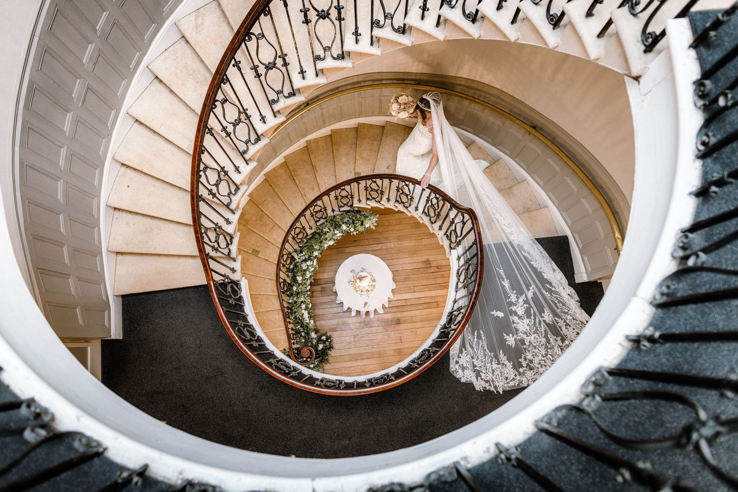 Bride and groom share a romantic kiss on a grand stone staircase lined with candles beneath a stained glass window.