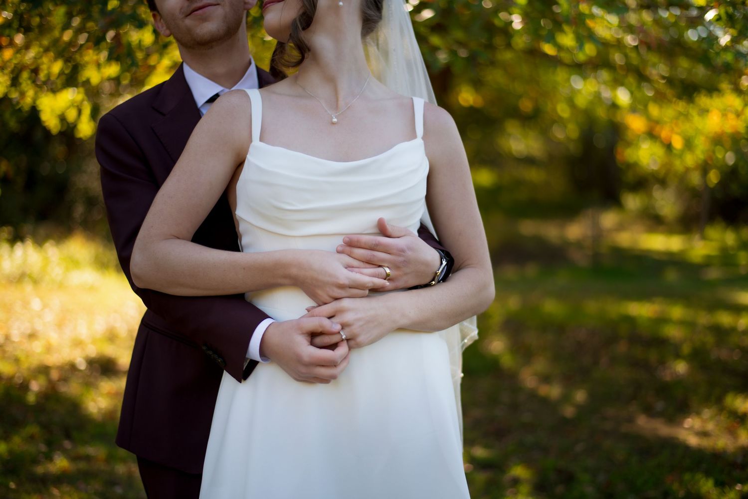 Bride and groom's hands with rings on wedding day. Outdoors with a green backdrop.