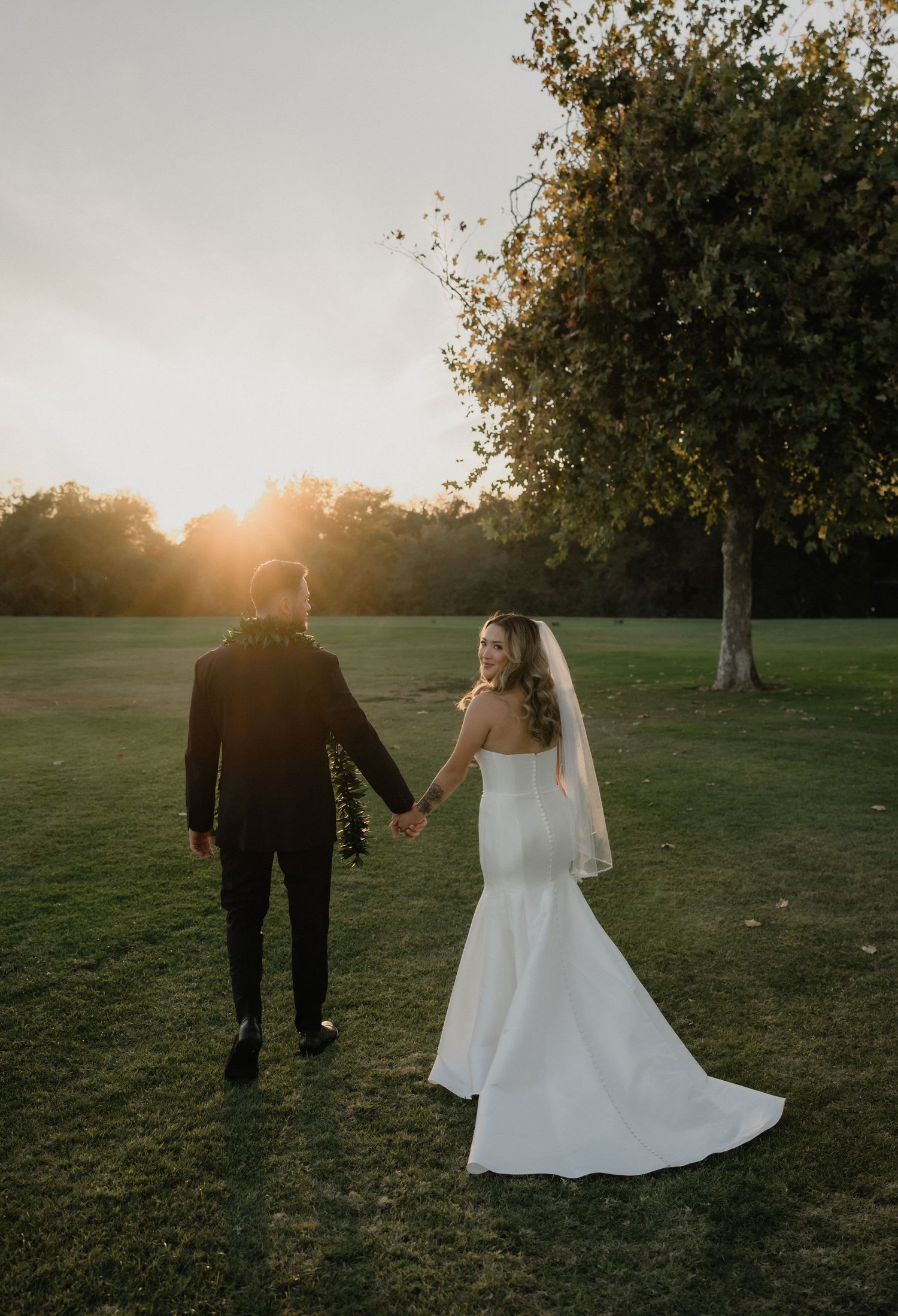 Black and white photo of bride and groom sharing an intimate moment under flowing wedding veil in outdoor field.