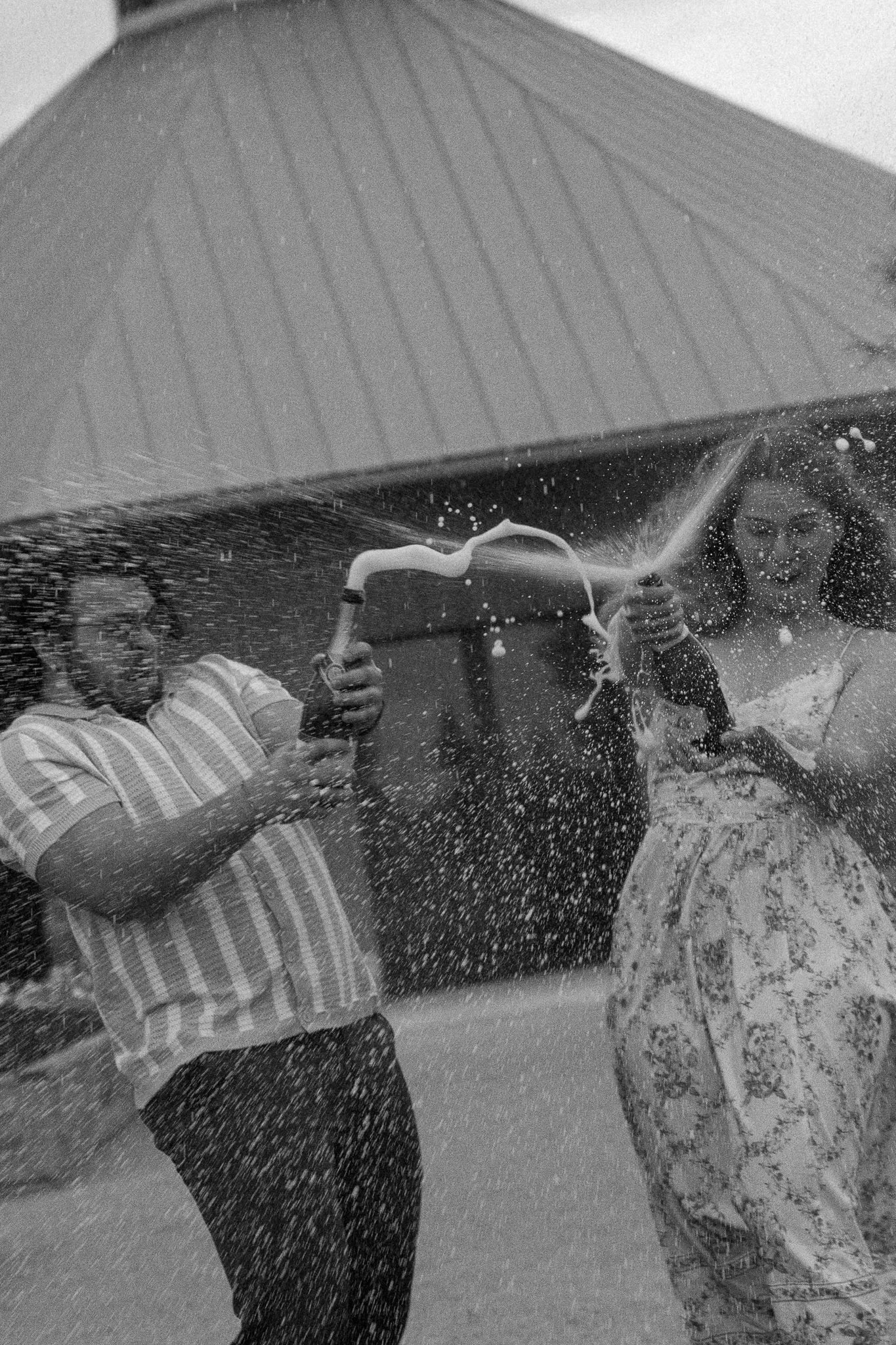 Black and white photo of a couple joyfully spraying champagne outside a building.