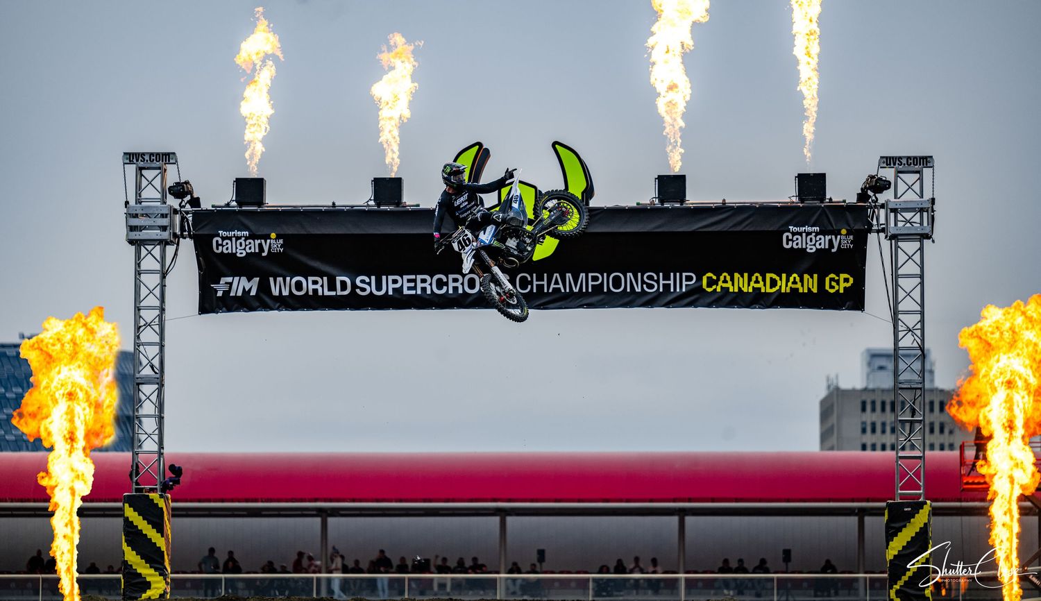 Motocross rider navigates a dirt track corner, spraying mud on a blue Monster Energy bike during an intense race.