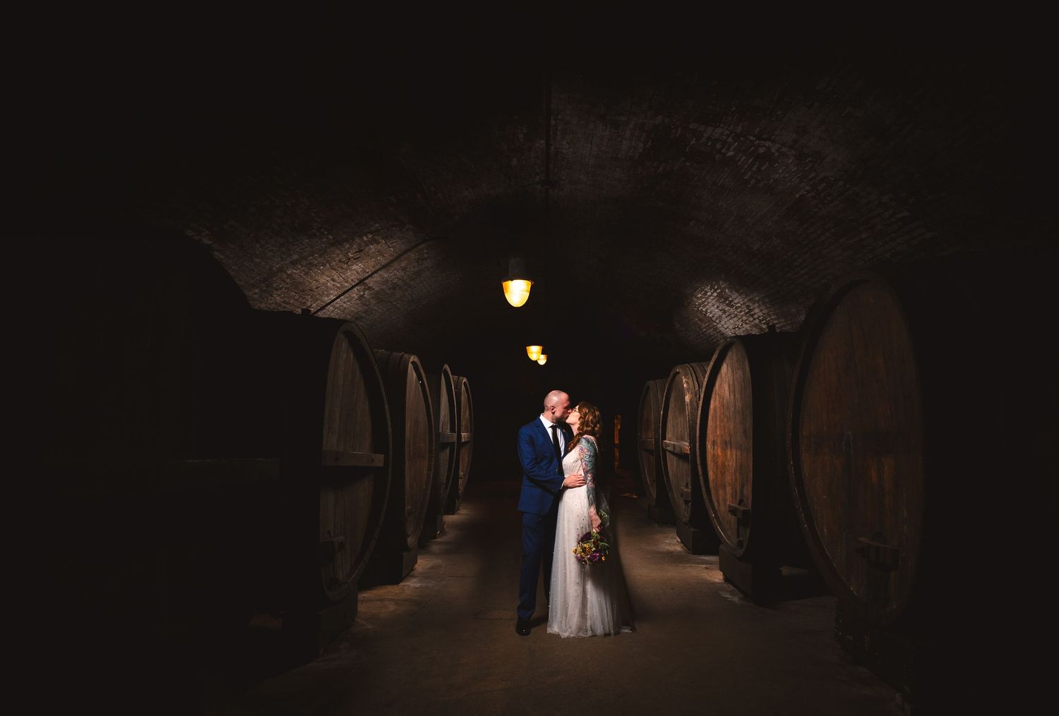Moody flash photo of couple kissing in historic wine cellar with barrels at Brotherhood Winery in Washingtonville, NY in the Hudson Valley.