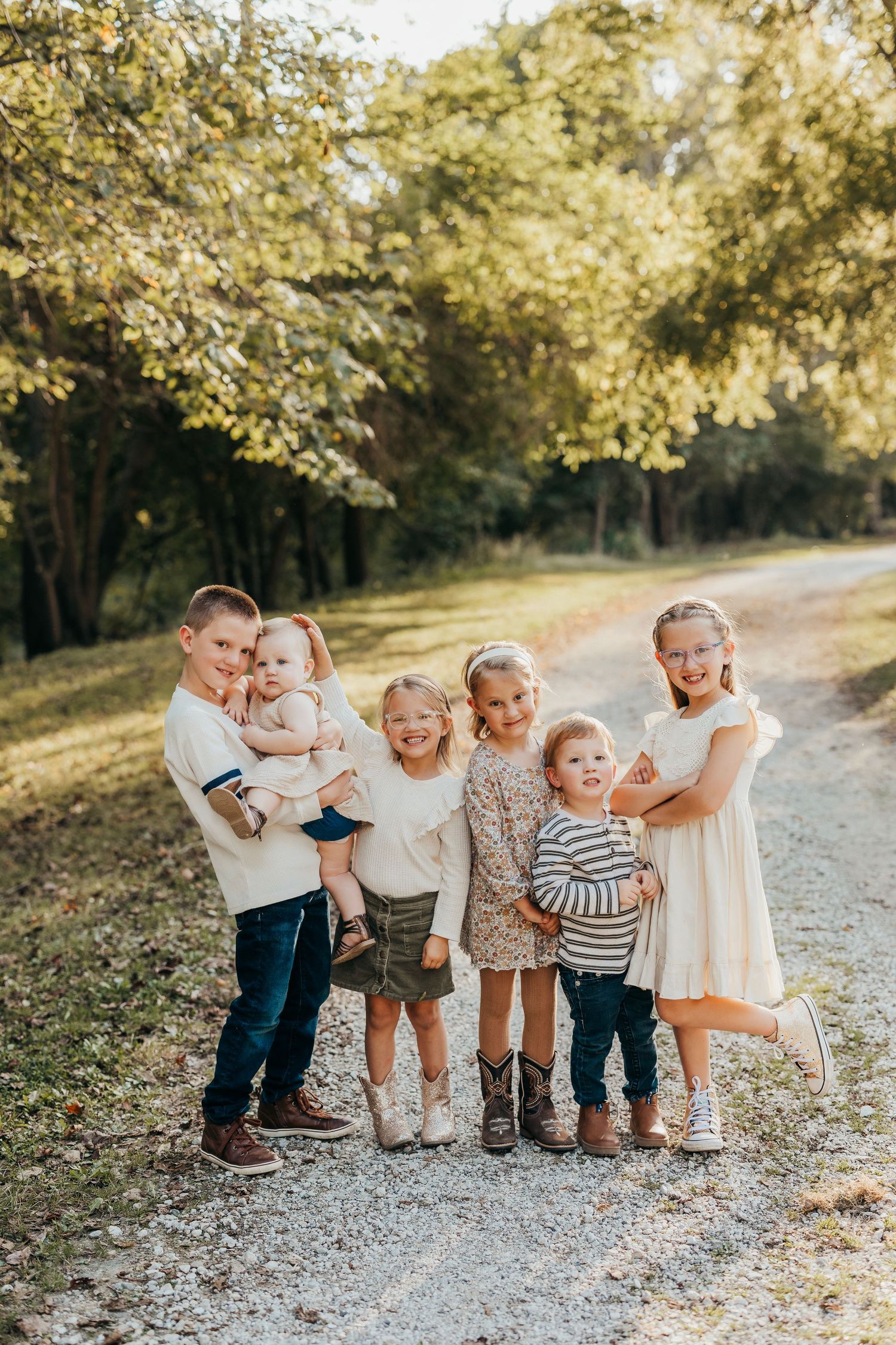 Group of young children in white and neutral colored outfits playing together on a sunlit gravel path in autumn.