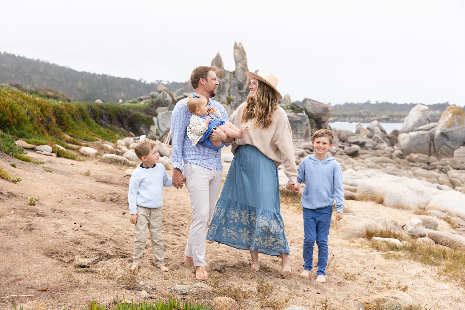 Family enjoying a coastal walk together on a rocky beach path with mountains and ocean in the background in Carmel By-the-Sea.