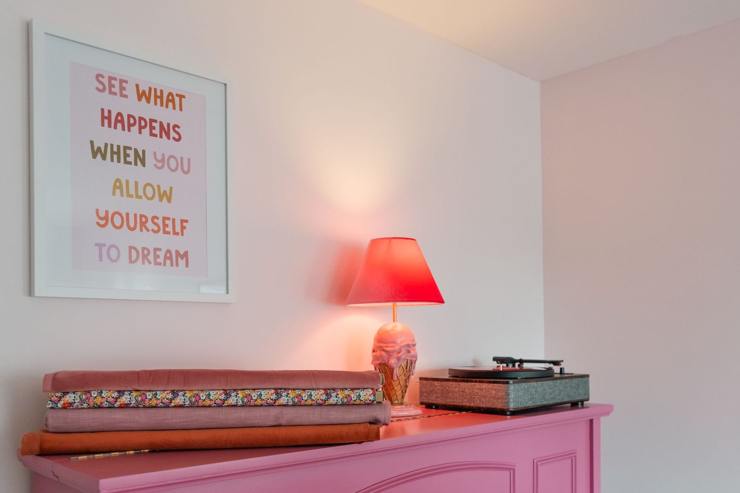 A pink dresser with a red lamp, record player, and artwork on the wall above it. A blog about what to know before you book your photoshoot.