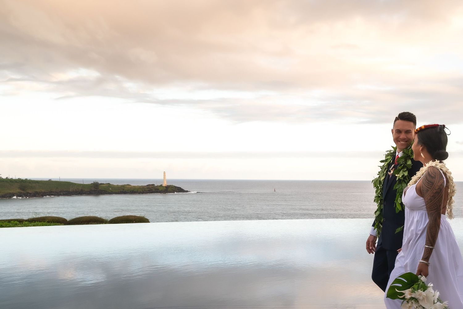 A romantic wedding couple stands silhouetted against a dramatic cloudy sky on a scenic coastal cliff.