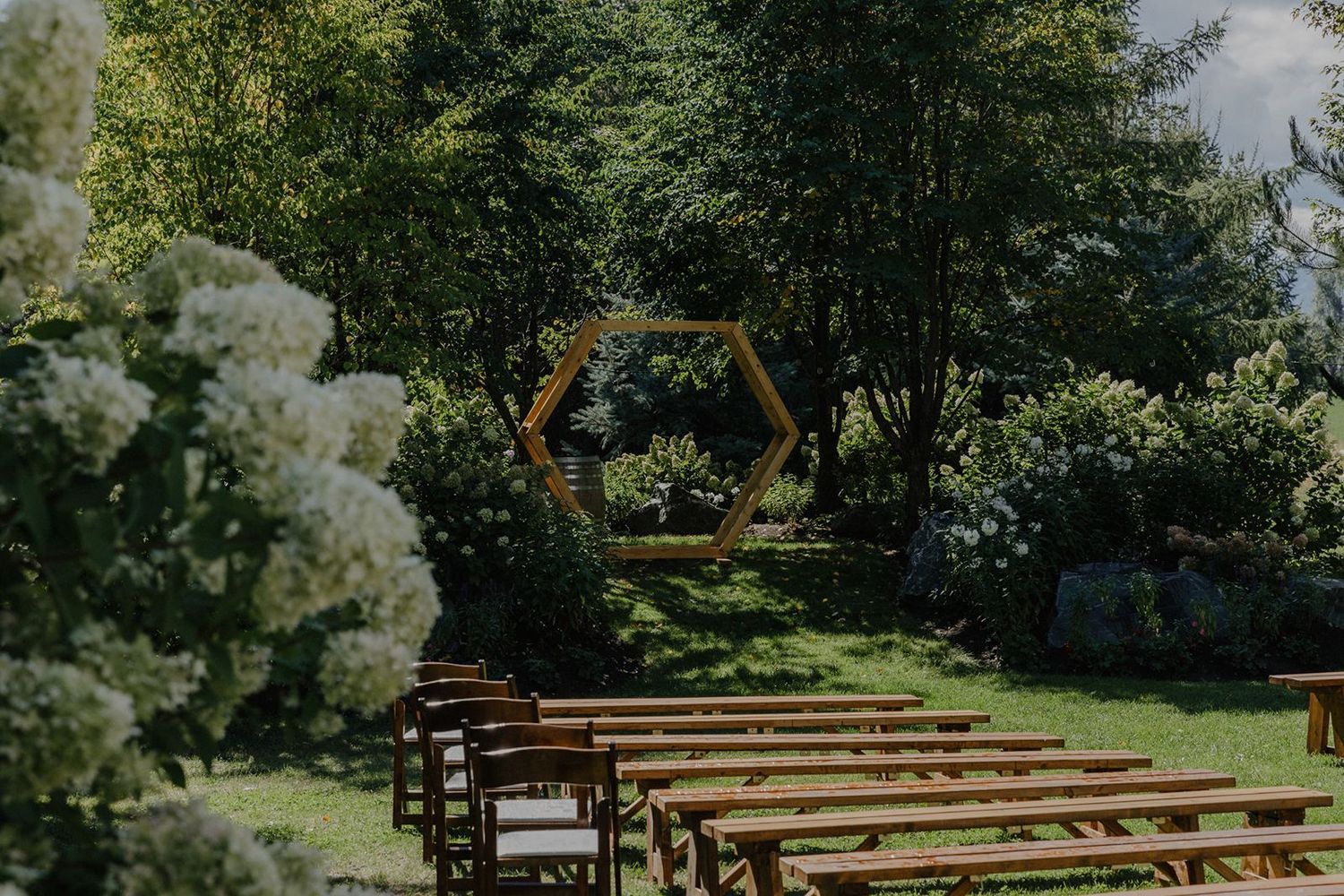 Elegant outdoor wedding ceremony setup with hexagonal arch framed by lush green trees.