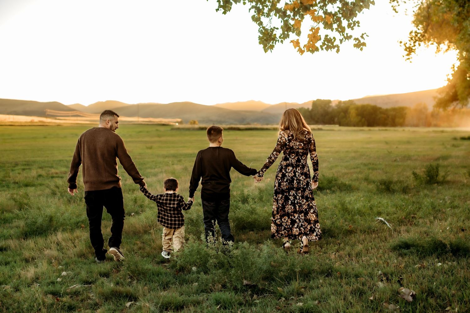 A family walks together through a sunlit meadow at golden hour creating a silhouette against the warm sky.