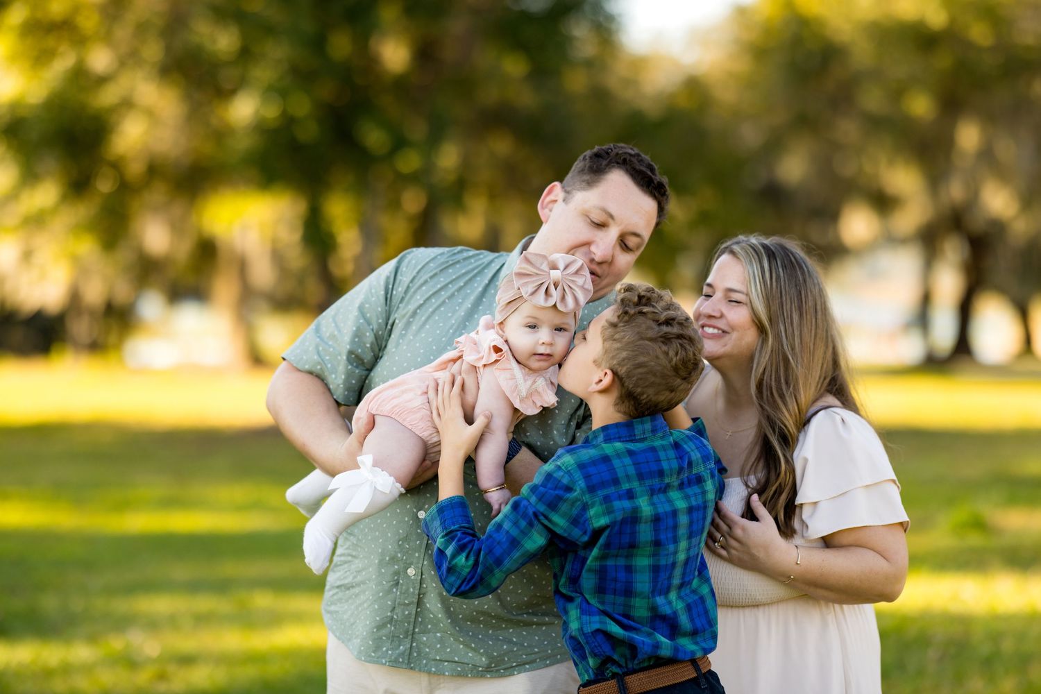 A family shares joyful moments together during a golden hour photo session in a sunlit park.