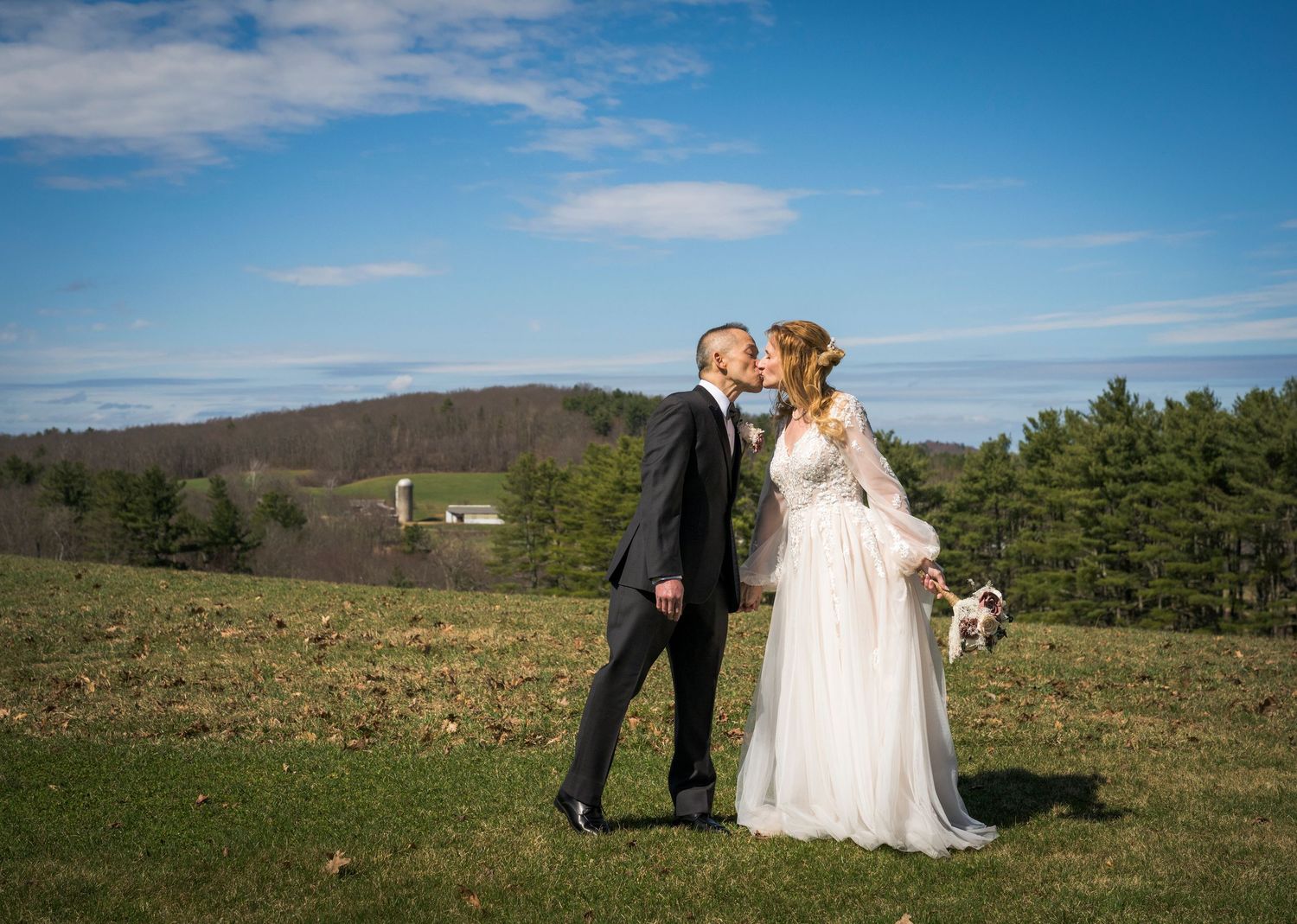 Newlyweds share an intimate moment outdoors with autumn foliage and rustic architecture in background.