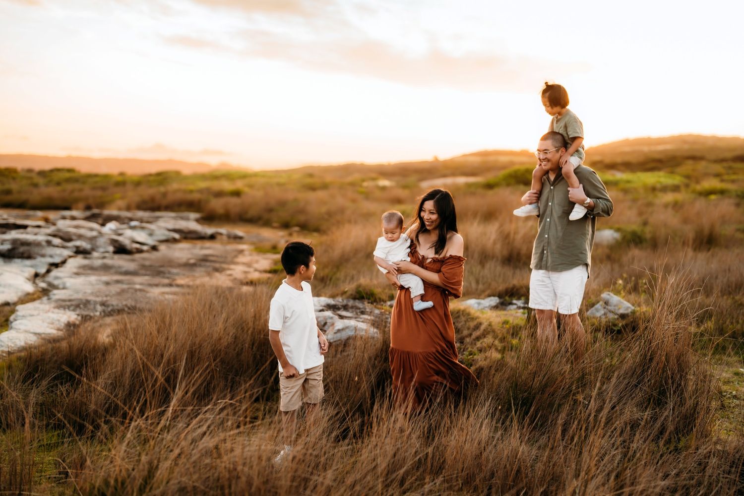 Family walking together through golden grass field during sunset photoshoot session in Sydney