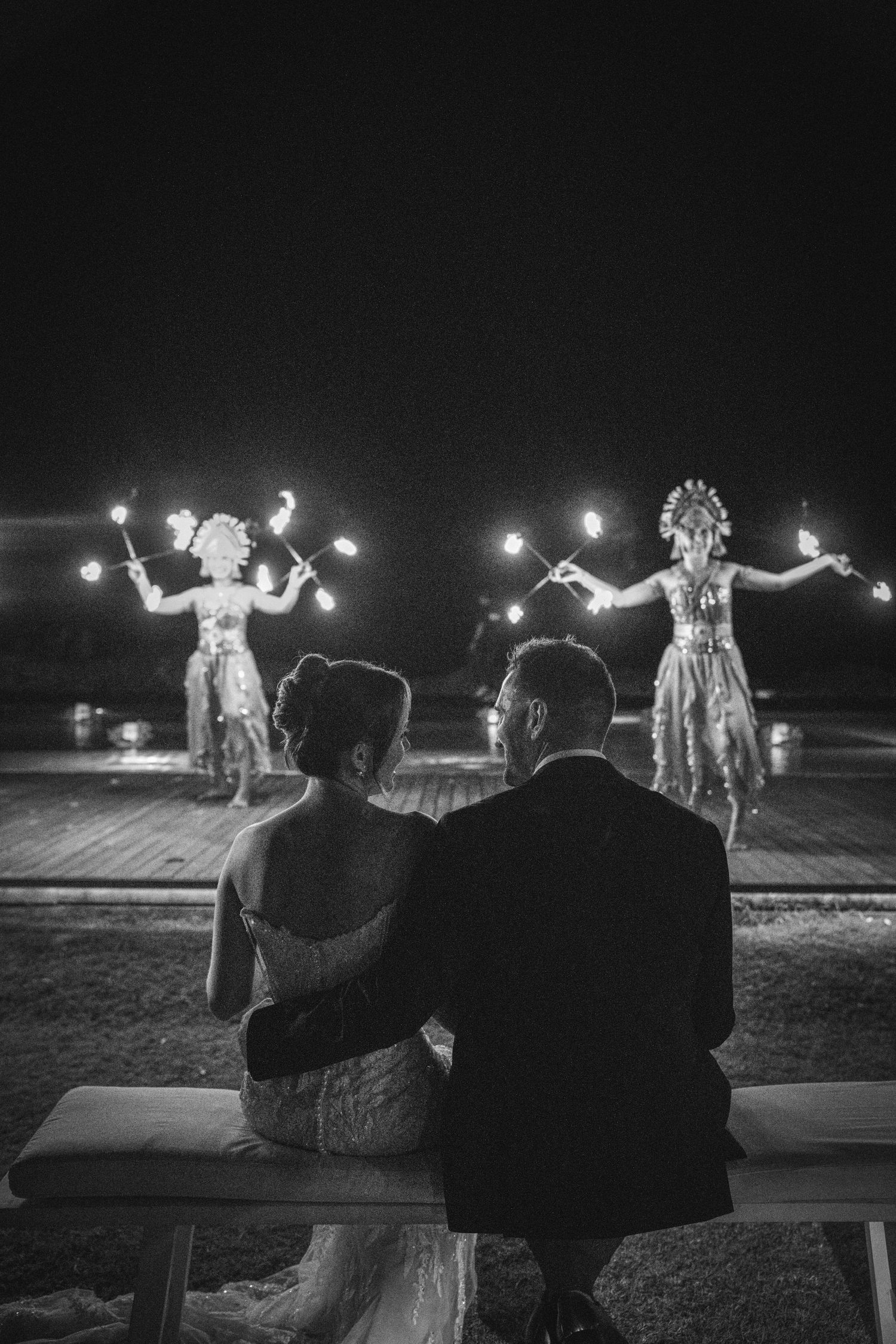 Silhouetted couple sharing a romantic kiss under flowing wedding veil at sunset with dramatic sky in background.