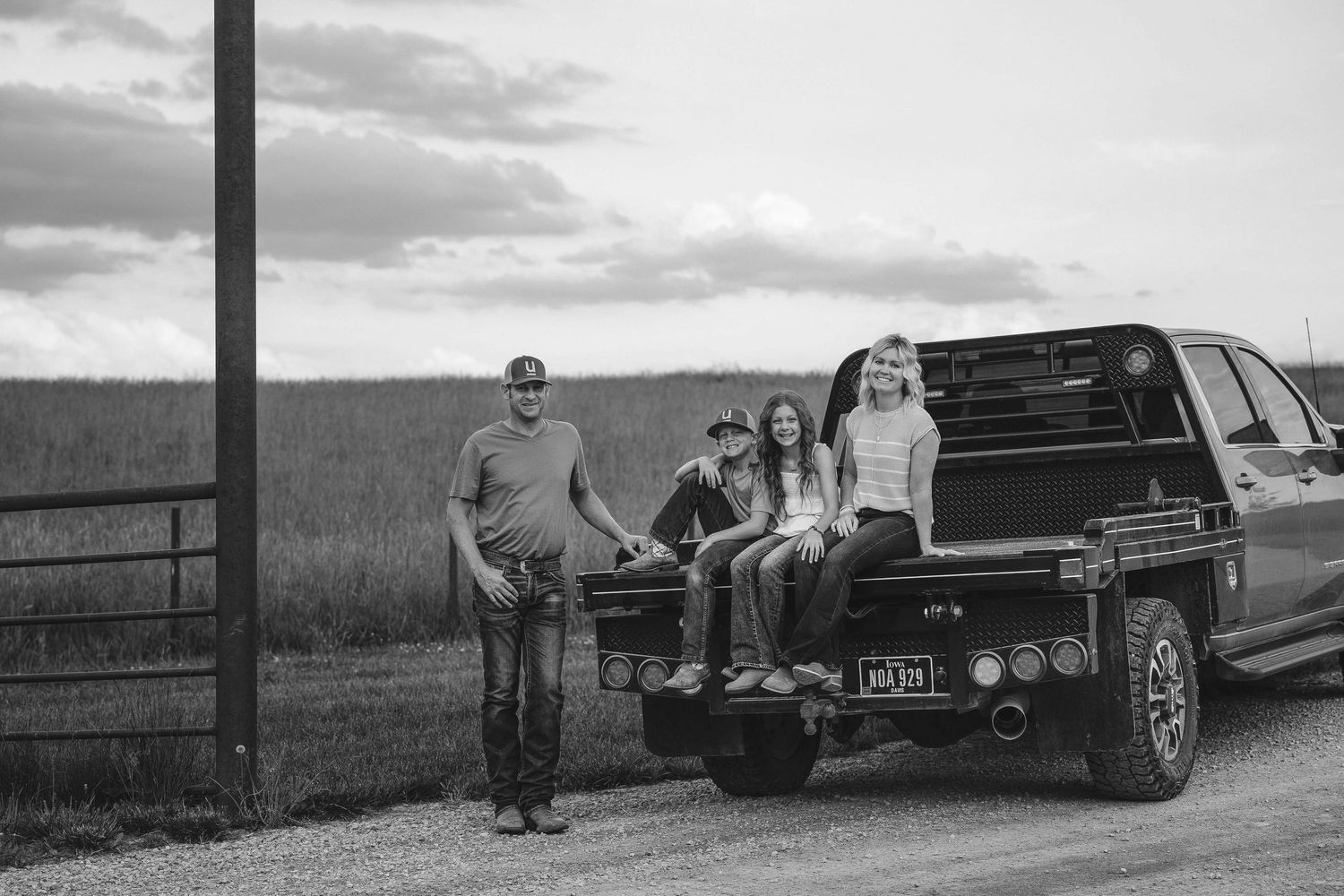 A group gathered around a black pickup truck parked on a dirt road at sunset in a rural setting.