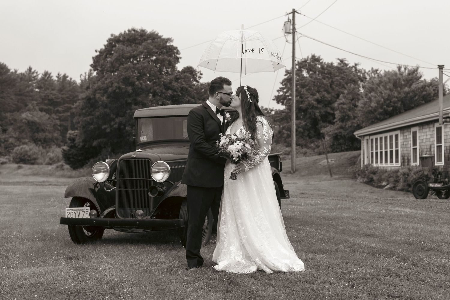 Wedding couple posing next to vintage green pickup truck in grassy field during outdoor countryside celebration.