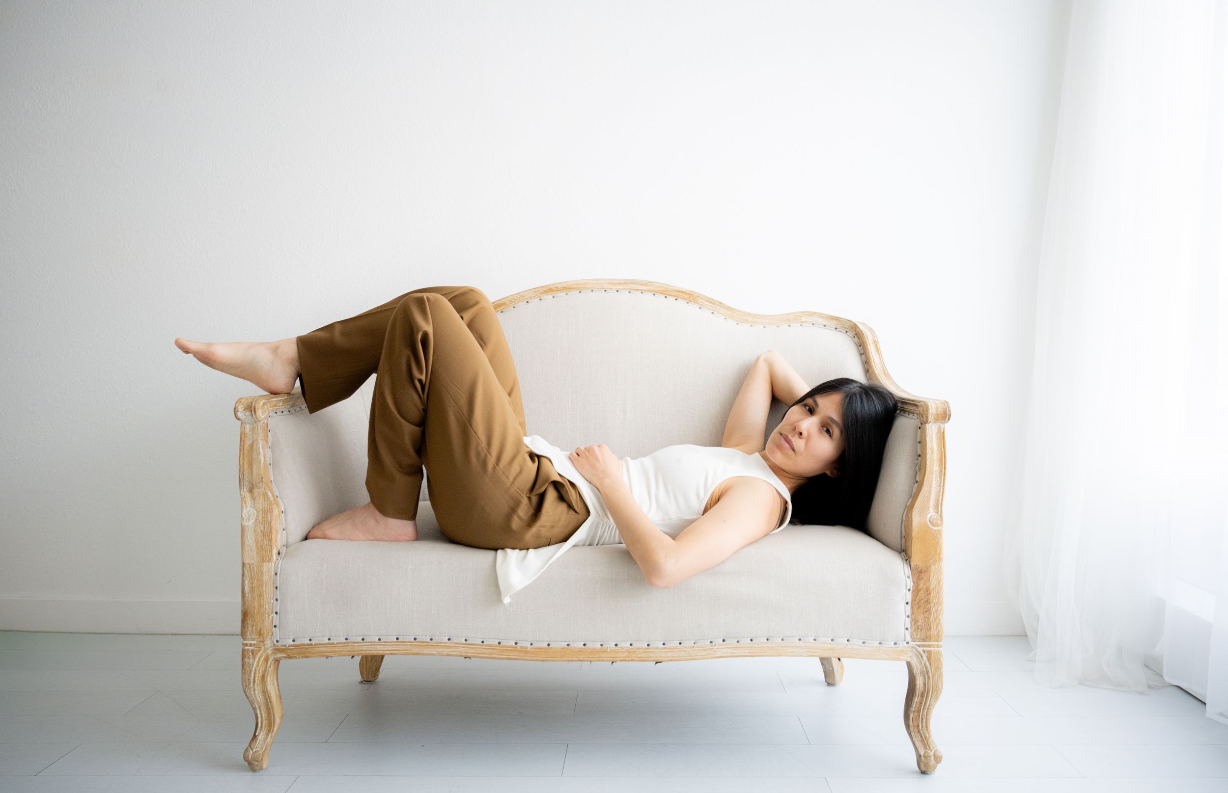 A person in brown clothing performs a dynamic floating pose sequence on a vintage wooden bench against a white wall.
