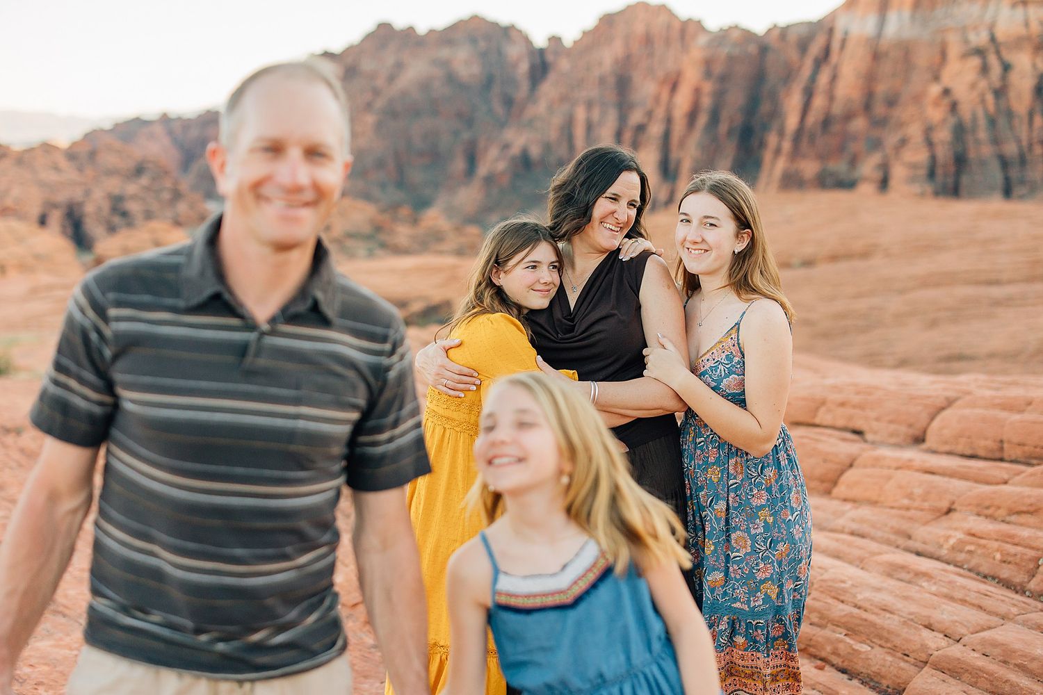 A family sits together on red rock formations in the desert landscape during sunset.