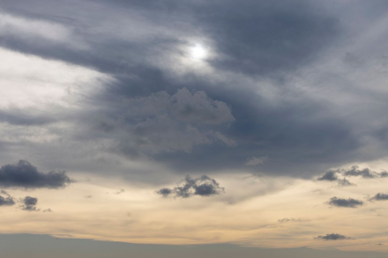 Dramatic cloudy sky with sun peeking through dark storm clouds against a golden sunset backdrop.