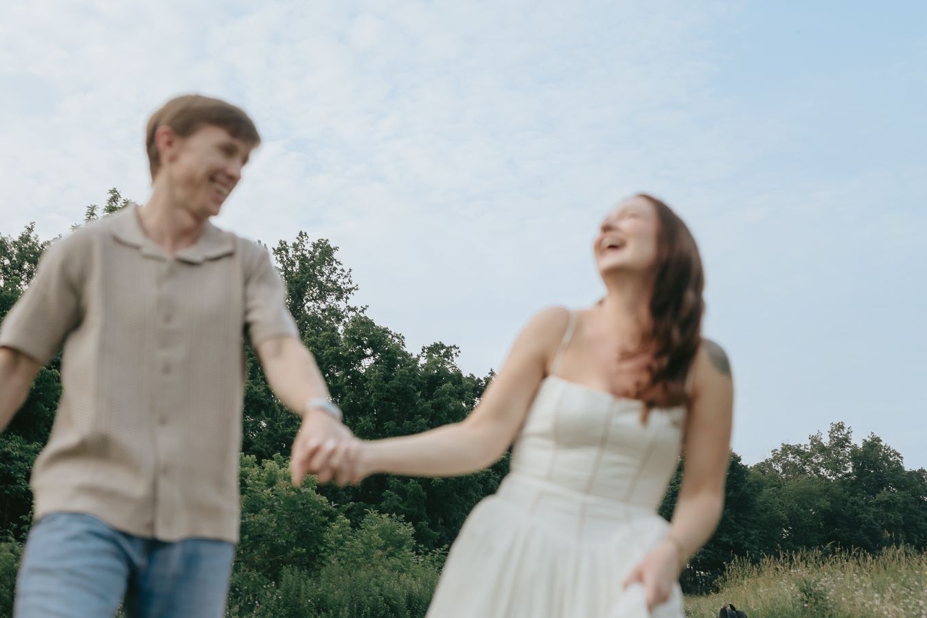 Couple laughing while holding hands in open field under a blue sky—joyful, natural, candid moment from NJ intimate wedding day photographer.