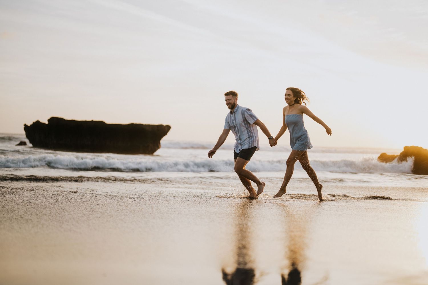 Couple enjoys a romantic beach photoshoot with waves crashing in the background.