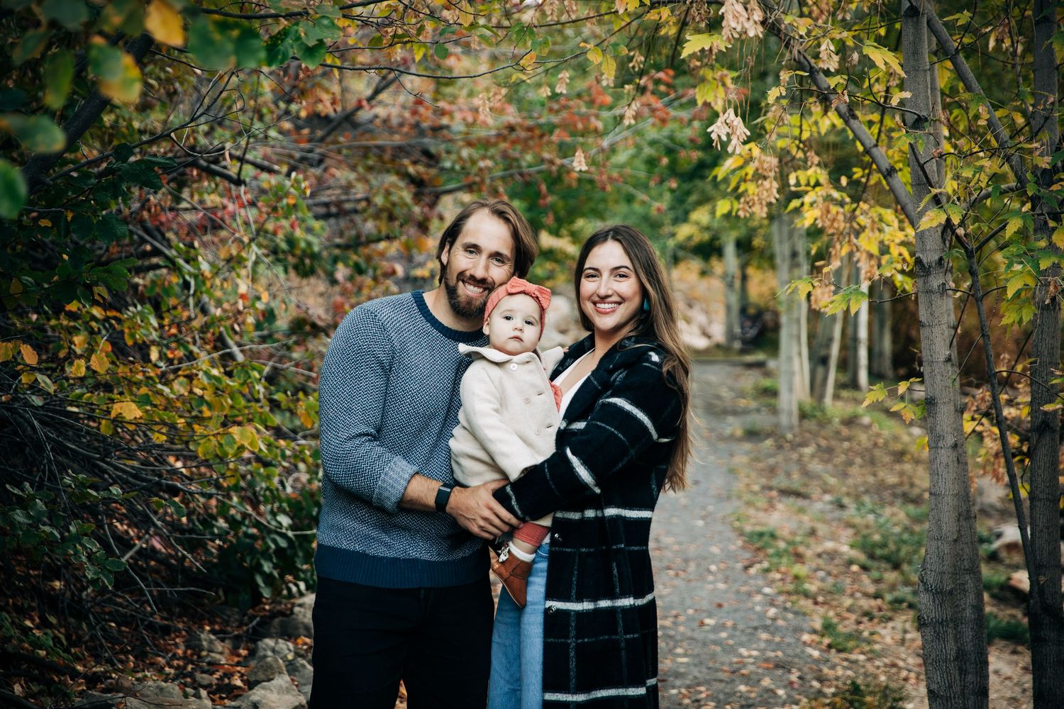 A family poses together in an autumn forest setting with golden leaves and natural lighting.
