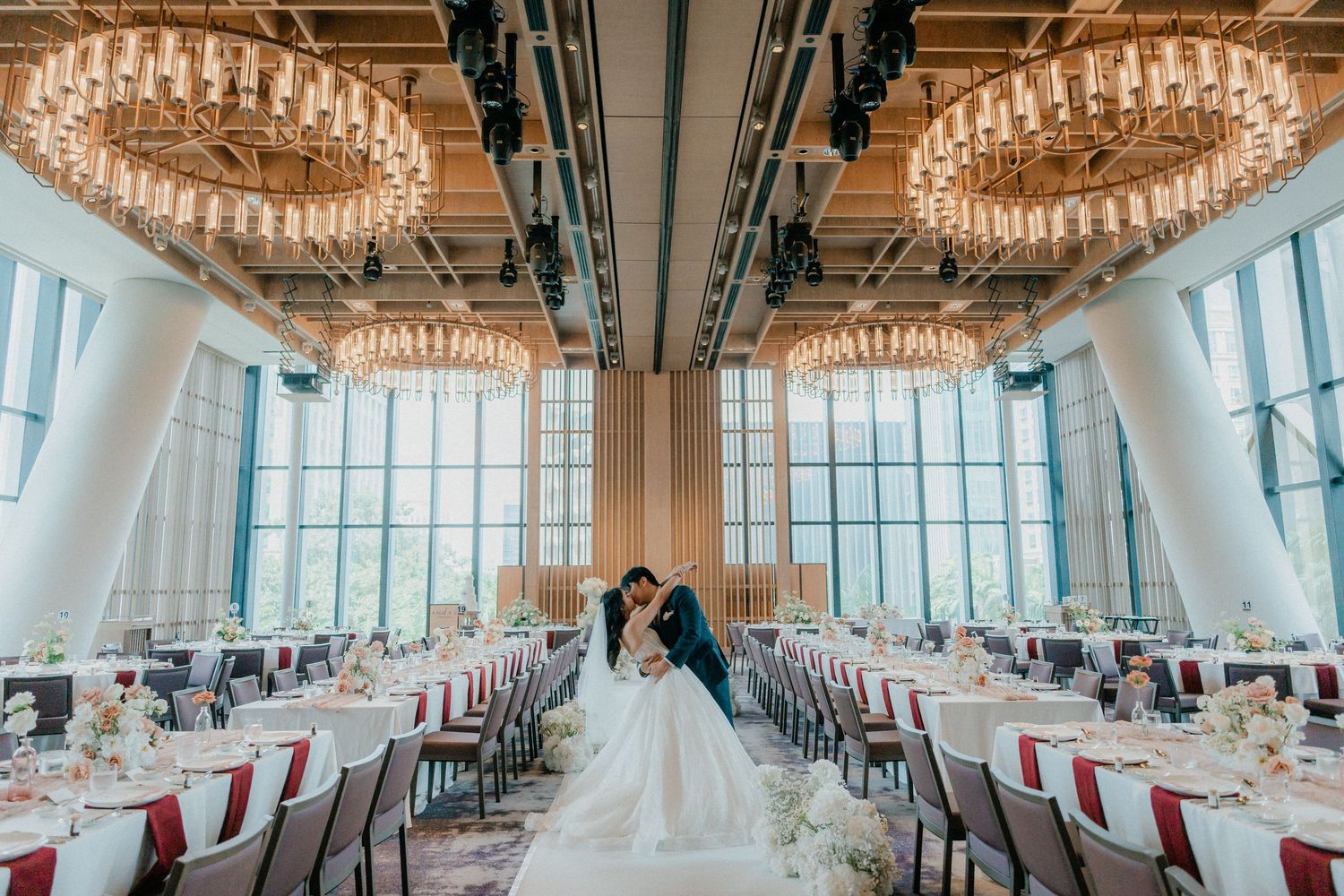Elegant banquet hall with crystal chandeliers and white table settings features panoramic windows and modern decor.