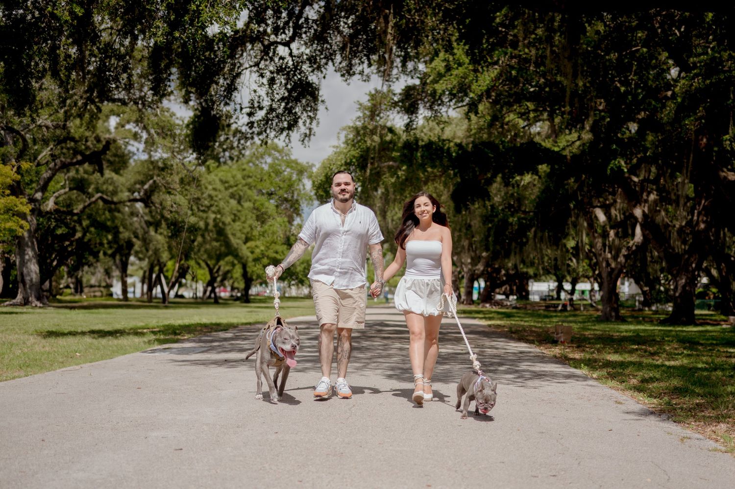 A couple strolls through a scenic tree-lined path at a serene park on a sunny day.