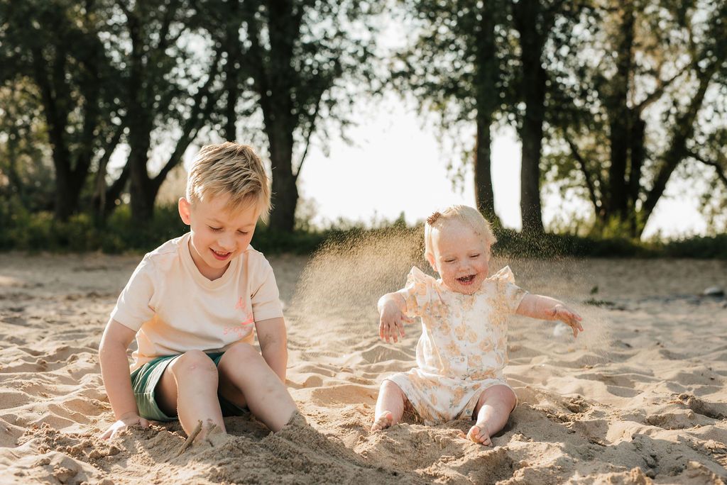 Two children play together in the sand during golden hour at the beach.