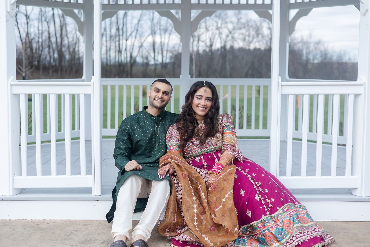 Couple in traditional South Asian attire posing in front of a white gazebo.