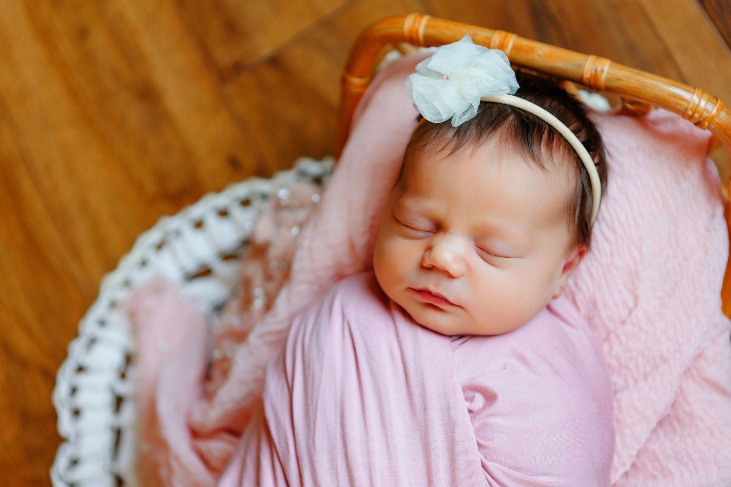Sleeping newborn baby wrapped in pink swaddle on lace blanket.
