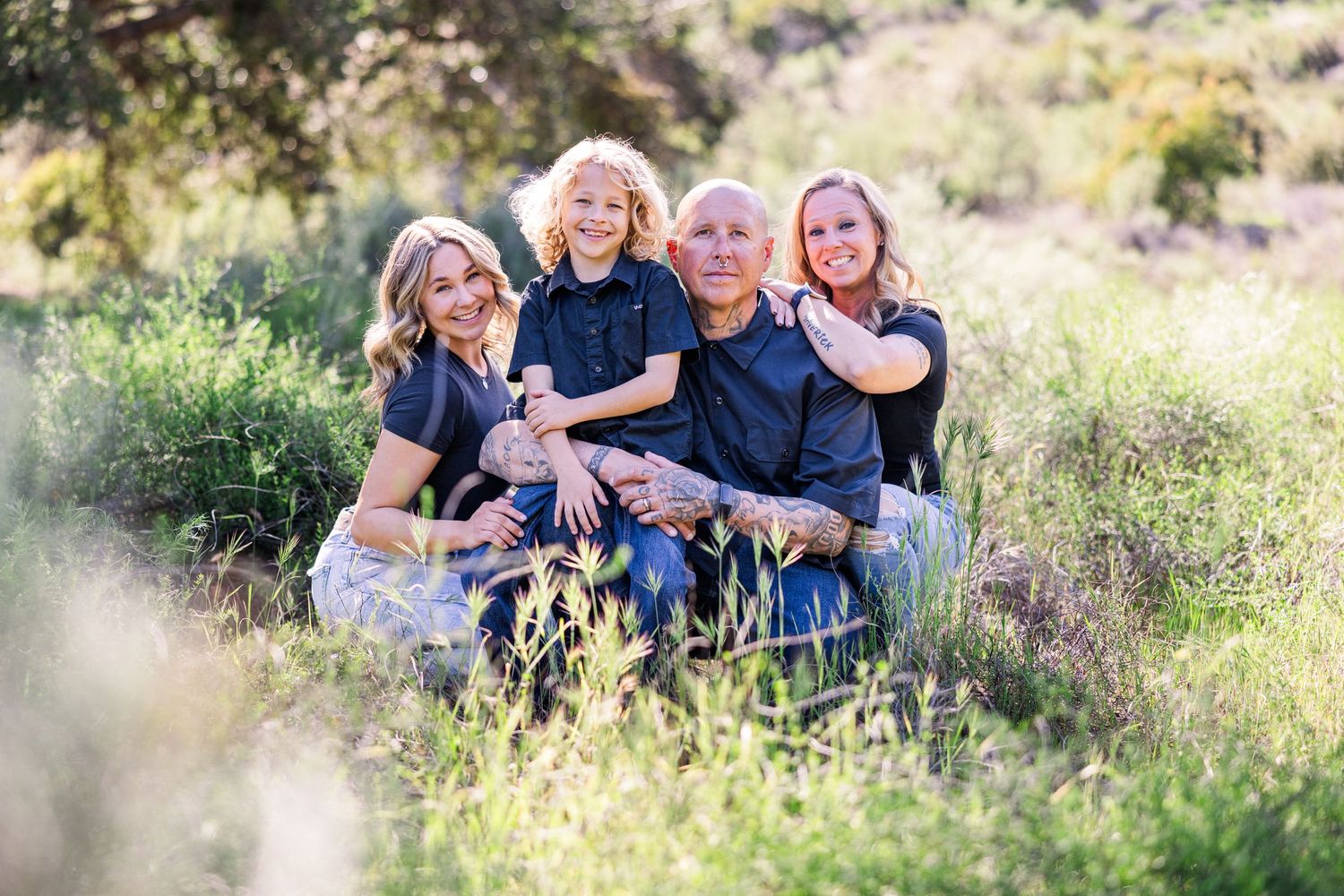 A family sitting together in tall grass outdoors during a casual photo session in nature.