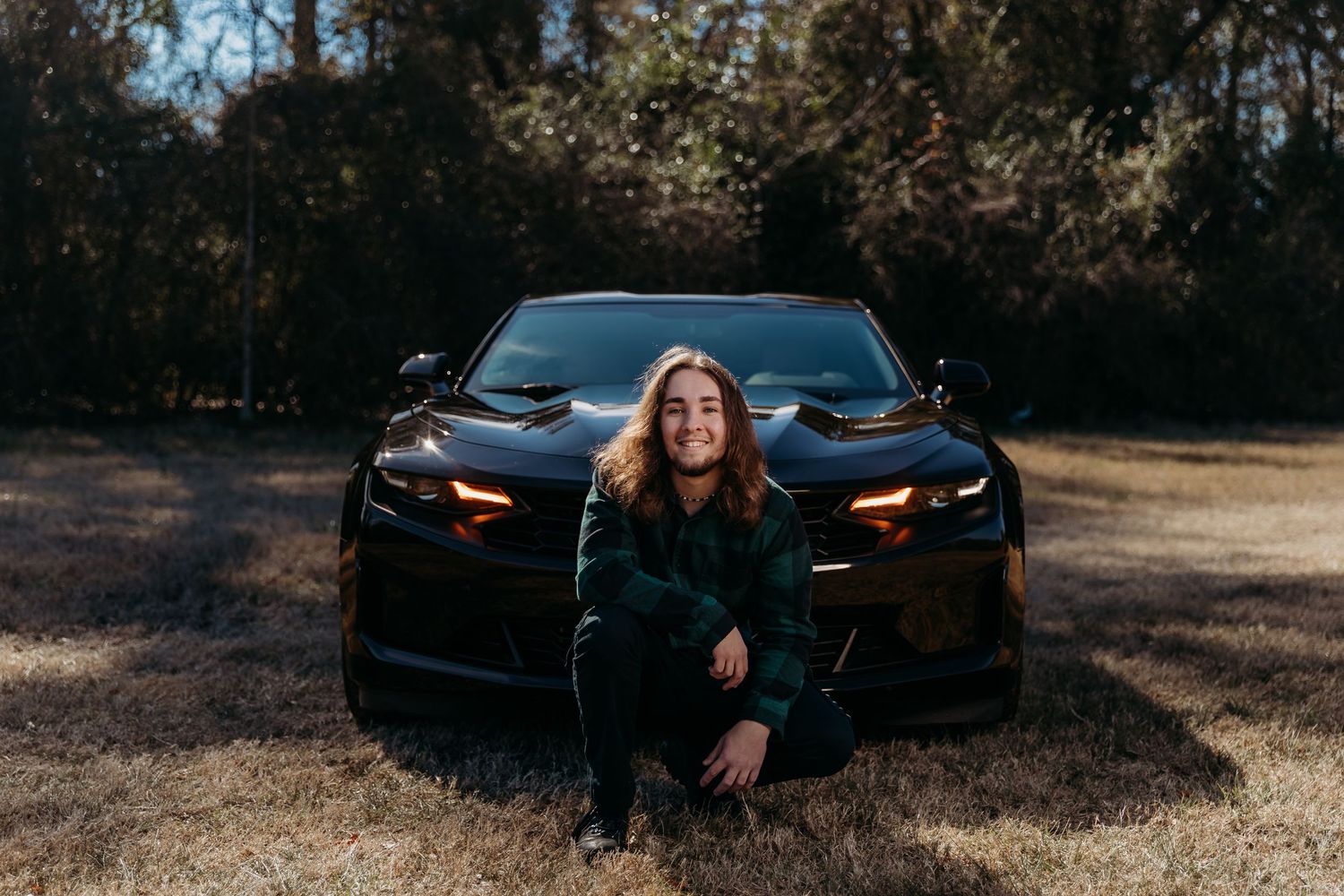 A sleek black Chevrolet Camaro parked on dirt ground with its headlights on at dusk.