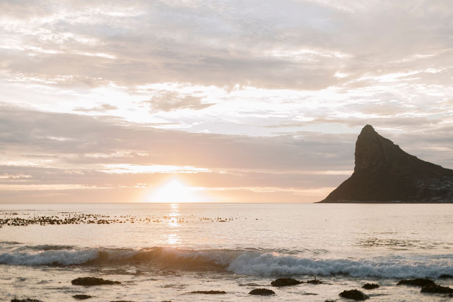 Golden sunset over the ocean with a dramatic rocky mountain silhouette on the horizon.