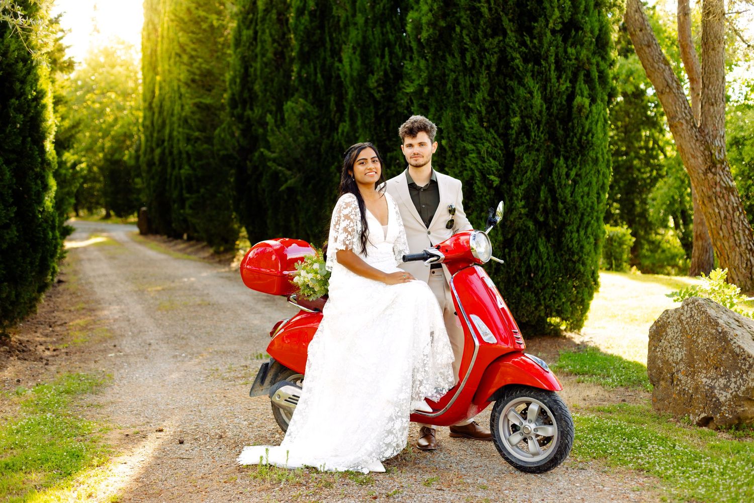 Red scooter parked on a tree-lined path with cypress trees and golden sunlight.