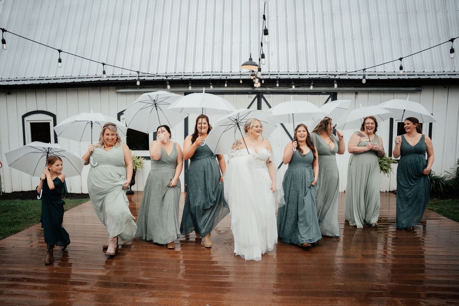 A joyful celebration on a rustic wooden deck in front of a white barn with string lights overhead.